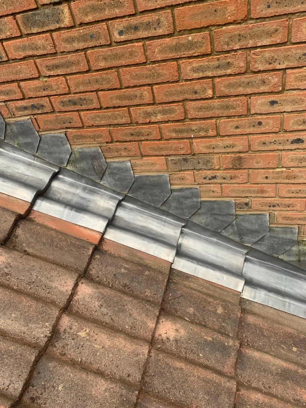 Stepped lead flashing tucked into brickwork above concrete roof tiles