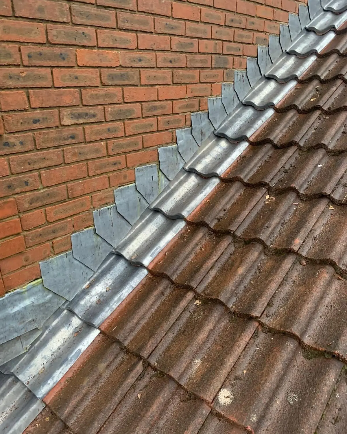 Ridge of a tiled roof fitted with new lead soakers against red brickwork