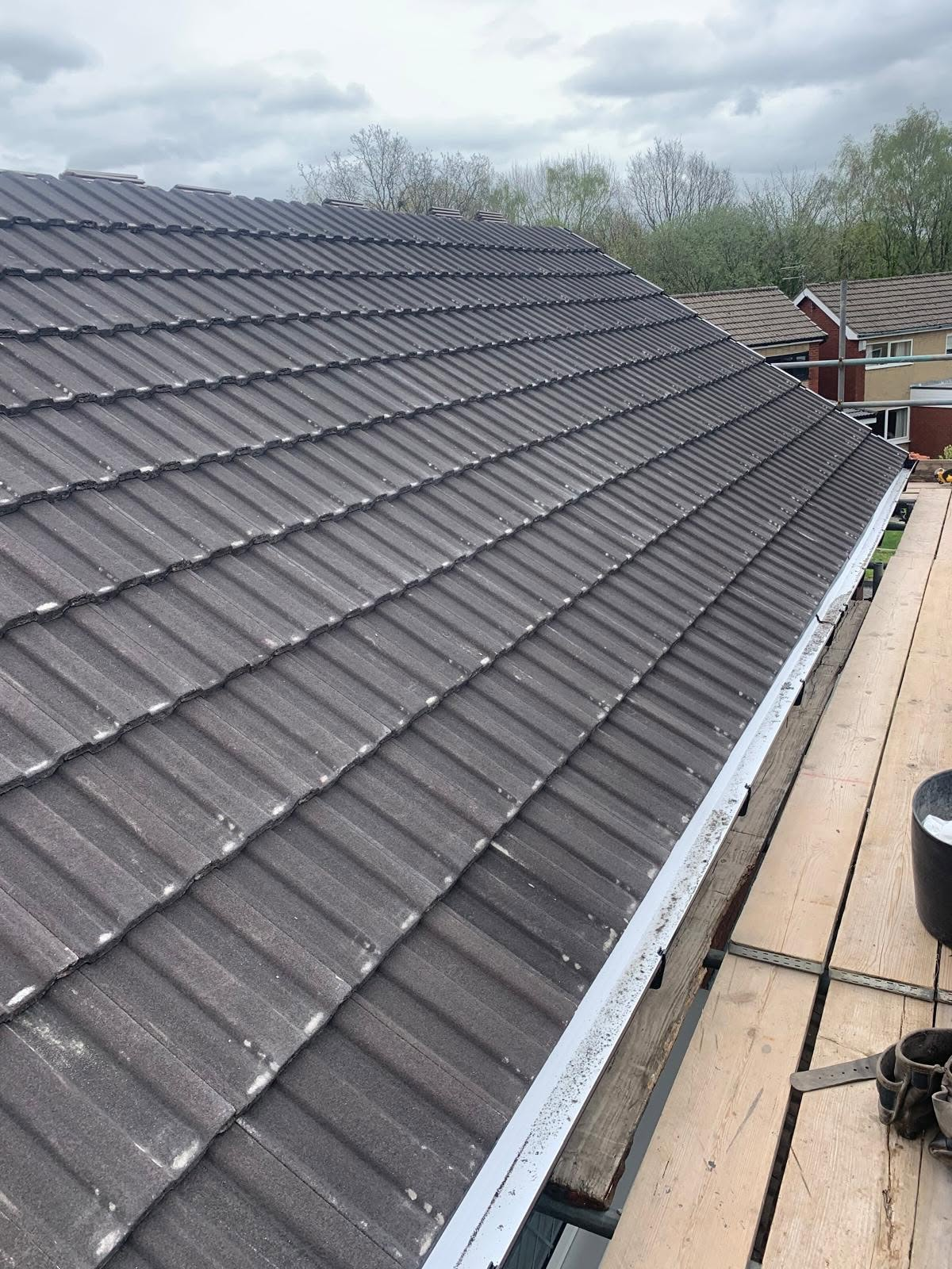 Concrete tiled roof and guttering seen along the eaves from scaffolding boards