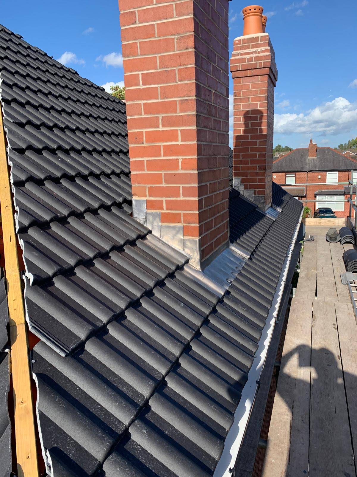 New dark tiled roof with two brick chimneys and stepped lead flashing, seen from scaffolding